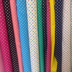 May include: A collection of colorful fabric rolls, each displaying a polka dot pattern. The fabrics vary in color, including pink, black, blue, green, yellow, and white, with dots in contrasting colors. Ideal for sewing and crafting projects.