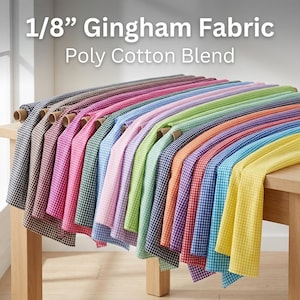 May include: A display of various colors of 1/8" Gingham fabric rolls. The fabric is a poly-cotton blend and is arranged on a wooden table. The colors include black, brown, pink, green, blue, and yellow.