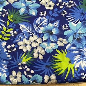 Puede incluir: Una tela vibrante con un estampado floral tropical. Grandes flores de hibisco azules y blancas se entrelazan con hojas verdes y azules sobre un fondo azul oscuro. El diseño incluye flores más pequeñas blancas y azules, creando un estampado botánico exuberante.