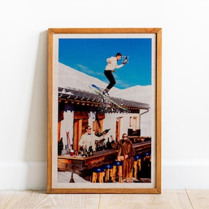 May include: A framed print shows a man on skis leaping over a bar, carrying a tray with bottles and glasses. A bartender pours drinks, and a person in a fur coat sits at the bar. The scene is set against a snowy mountain backdrop.