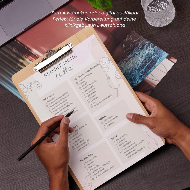 Peut inclure: Un presse-papiers en bois avec une liste de contr&ocirc;le en allemand intitul&eacute;e "KLINIKTASCHE". La liste comprend des sections pour les documents, le s&eacute;jour de la m&egrave;re, la naissance, l'allaitement, les extras et les articles pour b&eacute;b&eacute;. Un stylo est tenu au-dessus de la liste.