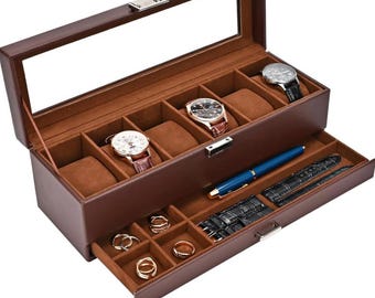 May include: A brown leather watch and jewelry box with a glass top. The top section holds five watches, while the bottom drawer contains rings, a pen, and watch straps. The interior is lined with a tan fabric.