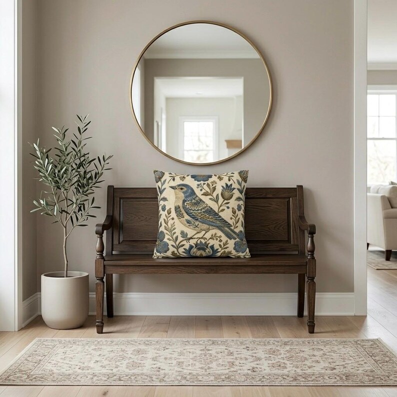 May include: A square throw pillow featuring a detailed illustration of a blue bird perched among stylized floral and botanical elements in shades of blue, brown, and cream, set against a light cream background with a textured fabric appearance.