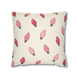 May include: A square throw pillow with an off-white background featuring a repeating pattern of pink and red light bulb illustrations. Each bulb has a small green base and is oriented in various directions across the fabric surface.