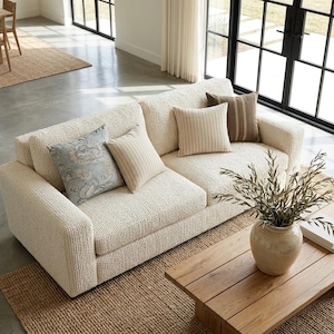 May include: A cream-colored textured sofa featuring two square throw pillows with vertical stripes, one square throw pillow with a blue and white floral pattern, and one dark brown striped throw pillow, all arranged on the seat cushions.