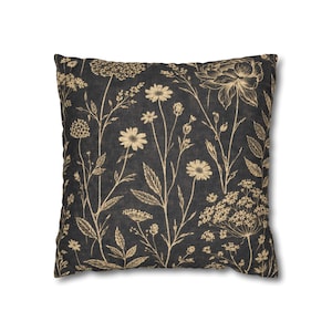 May include: Square throw pillow with a dark background and a beige floral pattern. The design features various wildflowers and foliage, creating a natural and botanical theme. The pillow is likely made of a soft fabric.