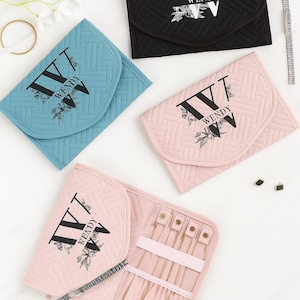 Op de afbeelding: Vier gewatteerde sieradenorganizers in zwart, blauw en roze. Elk heeft een klepsluiting en toont de naam "WENDY" met bloemen- en vlinderaccenten. Eén roze organizer is open en toont sieraden.