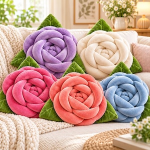 May include: Five plush throw pillows shaped like blooming roses in purple, cream, hot pink, coral, and blue. Each flower pillow features soft, velvet-like fabric petals arranged in a spiral pattern with green fabric leaves at the base.