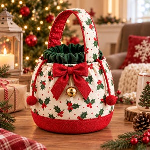 May include: A round fabric gift bag featuring a cream background with a red and green holly leaf and berry pattern. The bag has a dark green drawstring top, a red glittery base, a red glittery bow, and a gold jingle bell hanging from the centre.