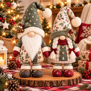 May include: Two plush gnome figurines standing on a wooden slice. The left gnome wears a green hat with white stars and a white beard. The right gnome features a cream hat with holly patterns, braided hair, and a green and plaid outfit.