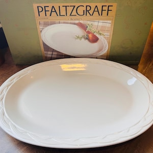 May include: Cream-colored oval serving platter with a decorative embossed border. The platter is part of the Pfaltzgraff "Acadia" collection, as indicated by the box in the background. The platter is a classic piece for serving food.