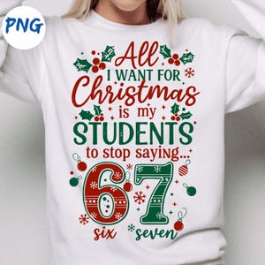 Op de afbeelding: Witte sweatshirt met een kerstthema. Het ontwerp toont de tekst "All I Want For Christmas is my STUDENTS to stop saying..." met de cijfers "67" in een feestelijke stijl. Rode en groene accenten.