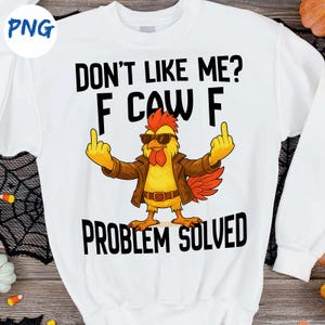 以下が含まれることがあります： 「DON'T LIKE ME? F CAW F PROBLEM SOLVED」の文字が入った白いスウェットシャツ。サングラスと茶色のジャケットを着た漫画の鶏が中指を立てています。
