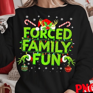 May include: Black sweatshirt with the text "FORCED FAMILY FUN" in green, decorated with Christmas lights, snowflakes, and candy canes. The design includes a Santa hat and Grinch-like hands holding ornaments. A festive holiday-themed top.