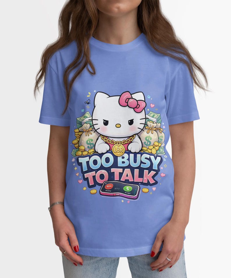 May include: A light blue t-shirt featuring a cartoon cat with a pink bow, gold chain, and the text "TOO BUSY TO TALK". The cat is surrounded by money bags and coins, with a smartphone graphic below.