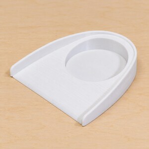 May include: A white plastic sorting tray with a smooth, rounded design featuring a wide, flat ramp leading into a circular recessed basin. The object has a clean, minimalist structure with visible horizontal layer lines from the manufacturing process.