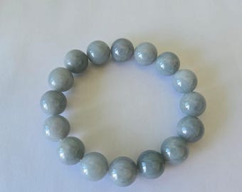 Könnte beinhalten: Ein Armband aus runden, hellgrauen Perlen. Die Perlen haben eine glatte, polierte Oberfläche und sind zu einer kreisförmigen Form aufgereiht. Das Armband wird vor einem weißen Hintergrund präsentiert.