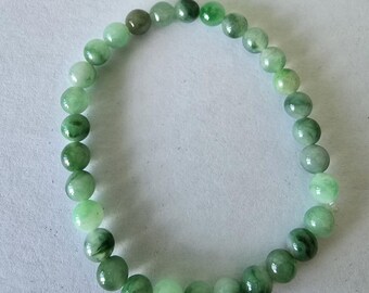 May include: A bracelet made of green jade beads. The beads are round and polished, with a glossy finish. The shades of green vary throughout the bracelet. The bracelet is strung together to form a complete circle.