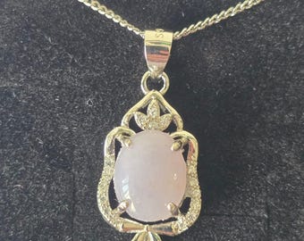 May include: A silver necklace with a pendant featuring a light pink oval gemstone. The pendant is encased in a decorative silver setting with small, sparkling accents. The chain is a delicate silver curb chain.