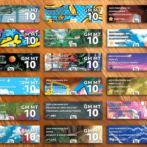 May include: A selection of graded Pokémon trading cards, each in a protective case with a "GM MT 10" grade. The cards showcase various Pokémon characters and sets, including Raichu, Charizard, and Eevee. The cards are displayed on a wooden surface.
