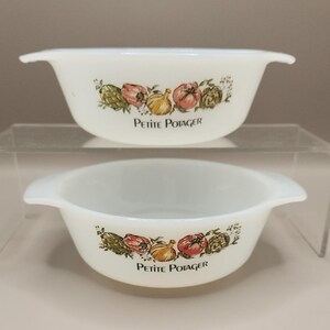May include: Two white, handled bowls with a decorative vegetable design. The bowls feature a floral pattern with artichokes, tomatoes, and onions. The text "Petite Potager" is printed below the design.