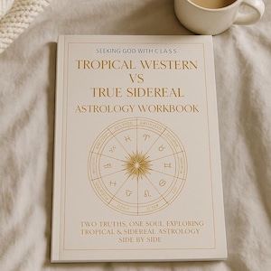 May include: A white astrology workbook with gold lettering and a circular zodiac design. The book's title is "Tropical Western vs True Sidereal Astrology Workbook." A white mug of coffee sits beside the book on a cream-colored surface.