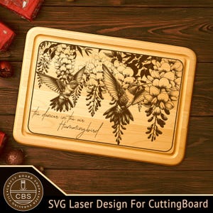 May include: A rectangular wooden cutting board with a laser-engraved design of hummingbirds and wisteria flowers. The text "The dancers in the air Hummingbird" is also engraved on the board. The board has a light wood finish.