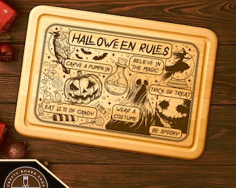 May include: A rectangular wooden cutting board with rounded edges. The board features engraved Halloween-themed illustrations and text, including a raven, pumpkin, ghost, and the words "Halloween Rules."