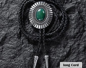 May include: A silver bolo tie with an oval green stone center and a decorative sunburst design. The black cord measures 42.5 inches/108cm long. The tips of the cord are silver with a decorative pattern. The text "long Cord" is visible.