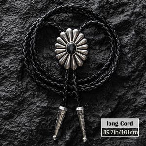 May include: A black bolo tie with a silver-colored flower-shaped pendant and a black stone center. The braided cord is black, and the tips are silver-colored. The cord length is 39.7 inches (101cm).