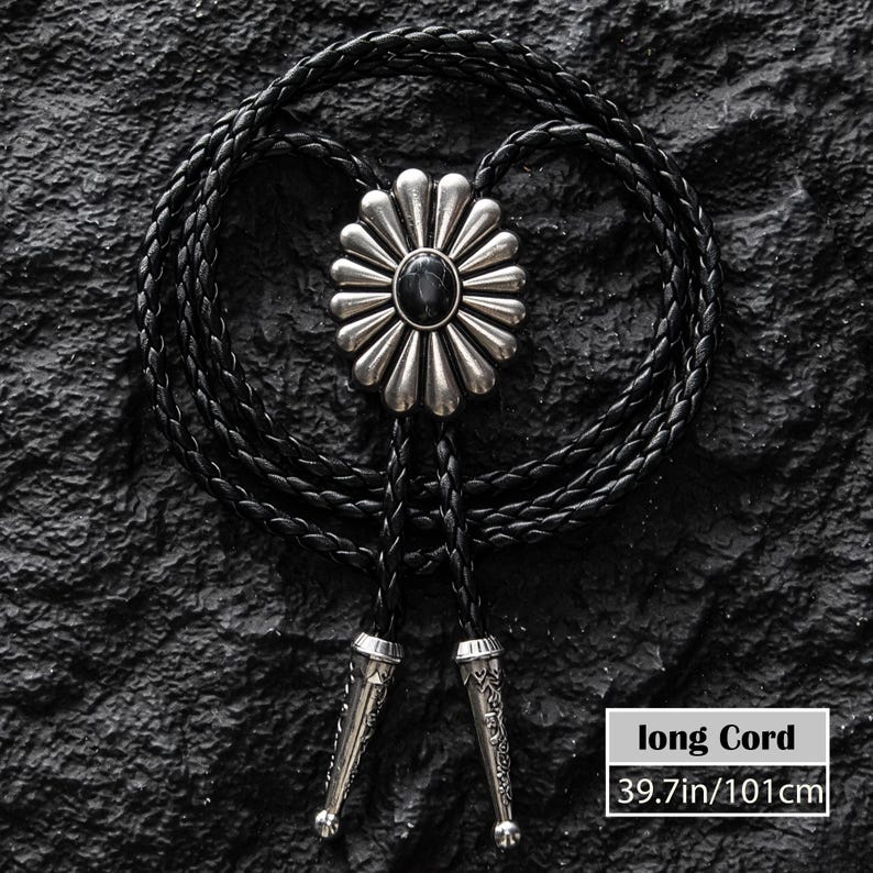 May include: A black bolo tie with a silver-colored flower-shaped pendant and a black stone center. The braided cord is black, and the tips are silver-colored. The cord length is 39.7 inches (101cm).