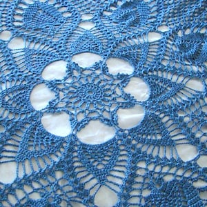 May include: A blue crocheted doily with a delicate floral pattern. The doily has a circular shape and is made with a fine thread.