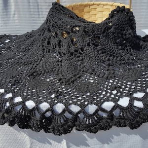 May include: Black crocheted table runner with a delicate lace pattern. The runner is circular and has a scalloped edge.