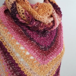 May include: A handmade, open-weave shawl in a triangular shape. The shawl features a gradient of colors, transitioning from orange to pink and deep purple. The yarn has a slight shimmer, adding a touch of elegance to the crocheted design.