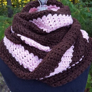 May include: A brown and pink crocheted infinity scarf. The scarf is made with a textured stitch and has a scalloped edge.