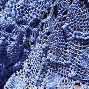May include: A close-up of a blue crocheted doily with a delicate floral pattern. The doily is made with a fine yarn and has a soft, airy texture.