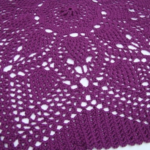 May include: A purple crocheted doily with a delicate, intricate pattern. The doily is circular and has a scalloped edge.