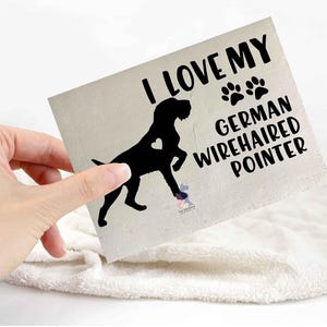 May include: A square, cream-coloured card held by a hand, with the text "I LOVE MY GERMAN WIREHAIRED POINTER" in black. A black silhouette of a dog with a heart cutout is also present, along with paw prints.
