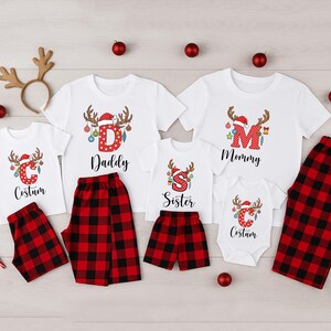 May include: Family Christmas pajamas set with white t-shirts and red and black plaid bottoms. The shirts feature reindeer antlers, Santa hats, and the words "Daddy", "Mommy", "Sister", and "Costum". Includes a reindeer antler headband.