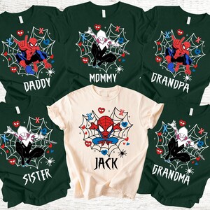 May include: A selection of green and cream t-shirts with Spider-Man and Spider-Gwen graphics. Each shirt is labelled with a family member's name: Daddy, Mommy, Grandpa, Grandma, Sister, and Jack. The designs incorporate spiderwebs, hearts, and spider illustrations.