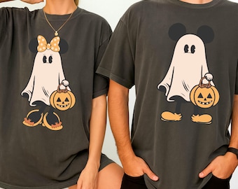 May include: Two dark grey t-shirts with a Halloween graphic. The design shows a cartoon ghost with Mickey Mouse ears holding a pumpkin. One ghost has a bow. The shirts have a relaxed fit.