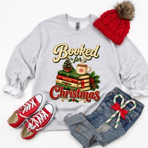 A gray sweatshirt with a graphic design, a red knit hat, red and white sneakers, a pair of blue jeans, and a pair of red and white candy canes.
