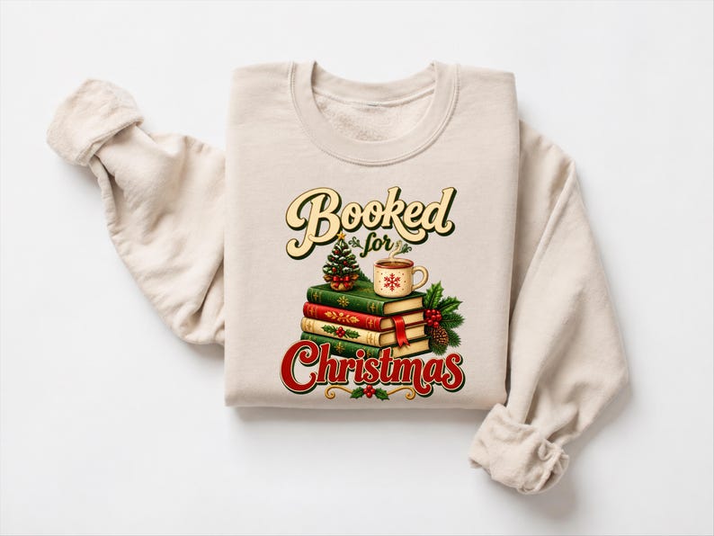 A beige sweater with a graphic design on it, featuring a stack of books, a mug, and a Christmas tree.