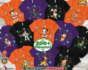 May include: A collection of short-sleeved t-shirts in orange, purple, and black, each featuring a Disney character surrounded by a string of colorful Christmas lights and blue snowflakes. Characters include Mickey, Minnie, Goofy, and others.