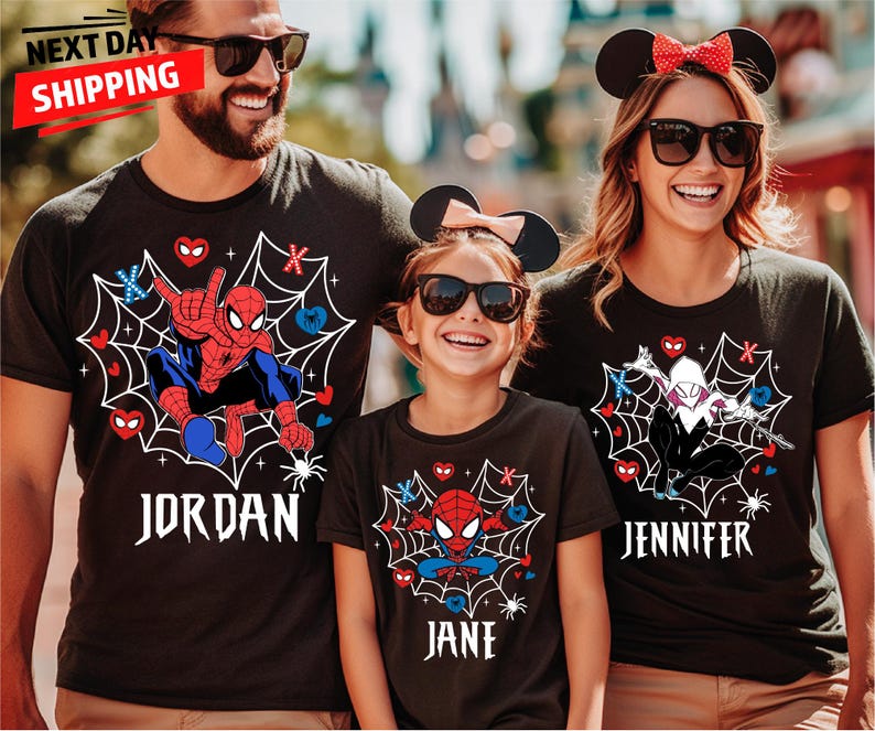 May include: Black t-shirts with Spider-Man and Spider-Gwen designs, personalised with names in a white gothic font. The shirts have a spiderweb graphic with hearts and spider accents. The family is wearing matching Mickey Mouse ears.