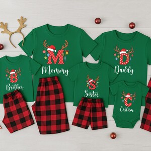 May include: A family Christmas pajama set in green with red and black plaid bottoms. The shirts have reindeer antlers and the letters "M", "D", "S", "C", and "B" with the words "Mommy", "Daddy", "Sister", "Costum", and "Brother".
