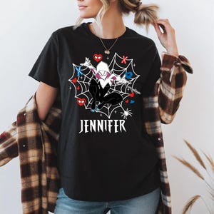 May include: Black t-shirt with a Spider-Gwen graphic in a spiderweb design, with red and blue heart accents. The name "JENNIFER" is printed in white below the graphic. The shirt has short sleeves.