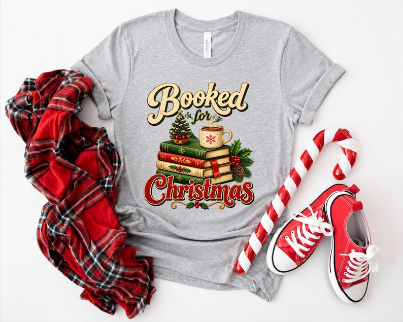 A gray t-shirt with a Christmas-themed graphic design, including a stack of books, a mug, and a Christmas tree, along with a pair of red and white striped candy canes and a red and white plaid shirt.