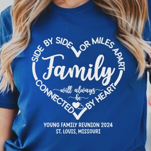 May include: A royal blue short-sleeved t-shirt featuring a white heart-shaped graphic with the text "SIDE BY SIDE OR MILES APART FAMILY WILL ALWAYS BE CONNECTED BY HEART" and "YOUNG FAMILY REUNION 2024 ST. LOUIS, MISSOURI" printed in white lettering.