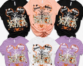 May include: Six short-sleeved t-shirts in black, peach, white, and lavender colours. Each shirt features a graphic of a Mickey Mouse-shaped outline containing a tree, ghosts, and cartoon characters dressed as mummies, with the text Name, BOO!!, and 2026.